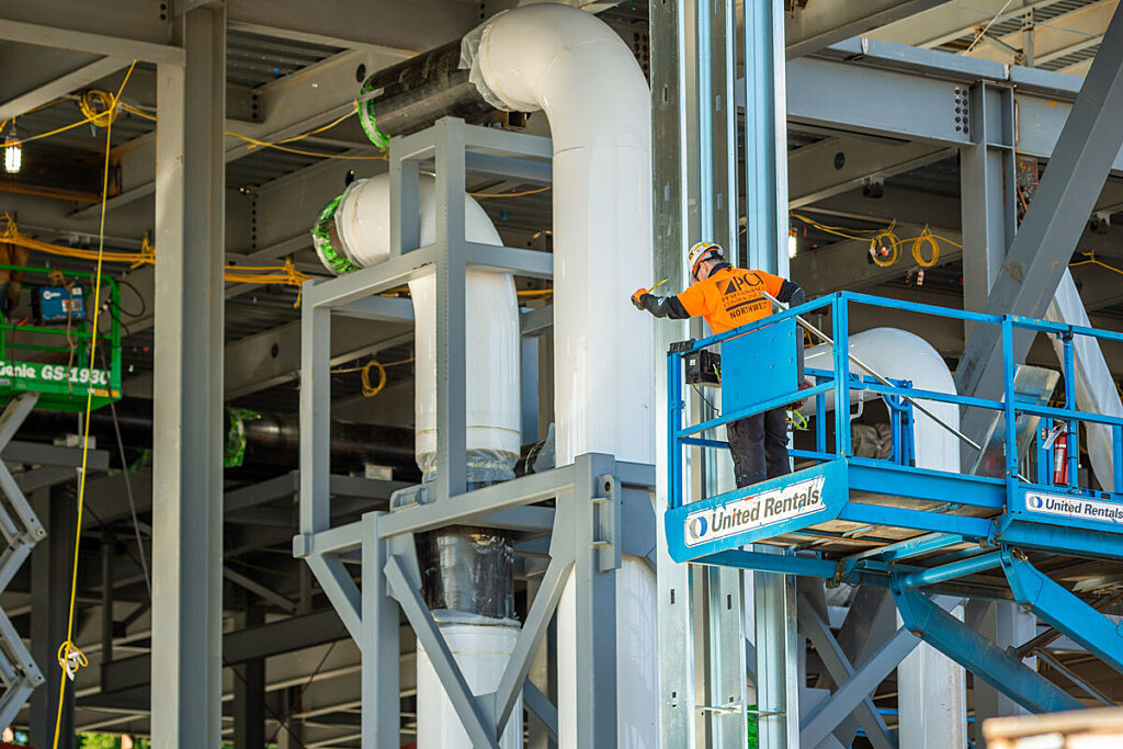 Construction worker on lift examining mechanical equipment.