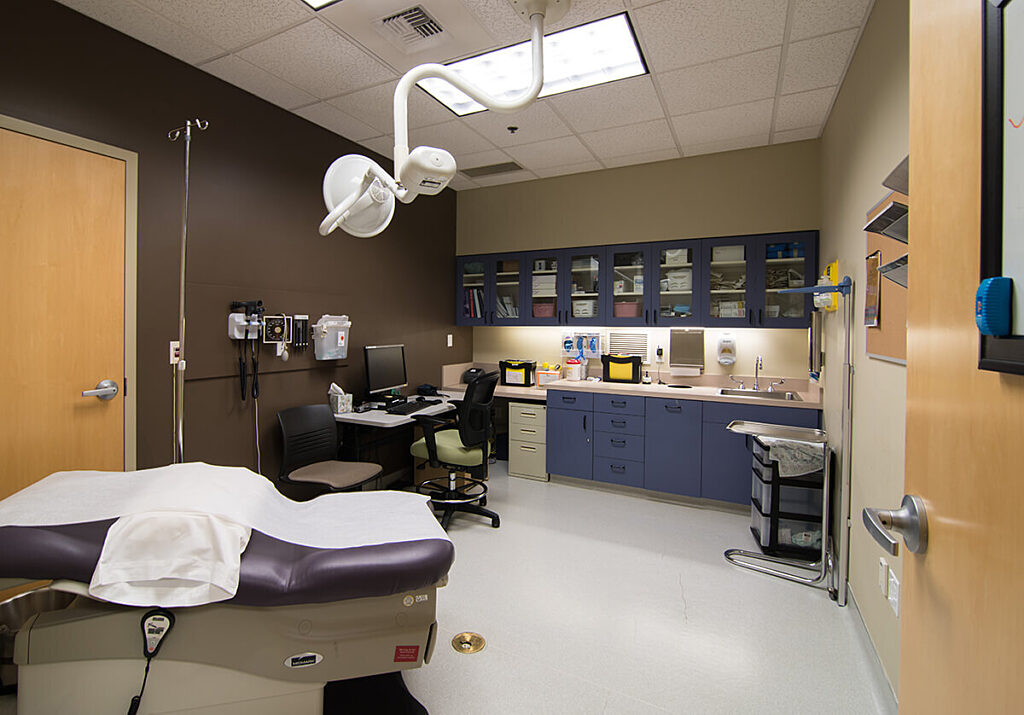 patient room at medical clinic with medical exam table and cabinets full of tools and supplies