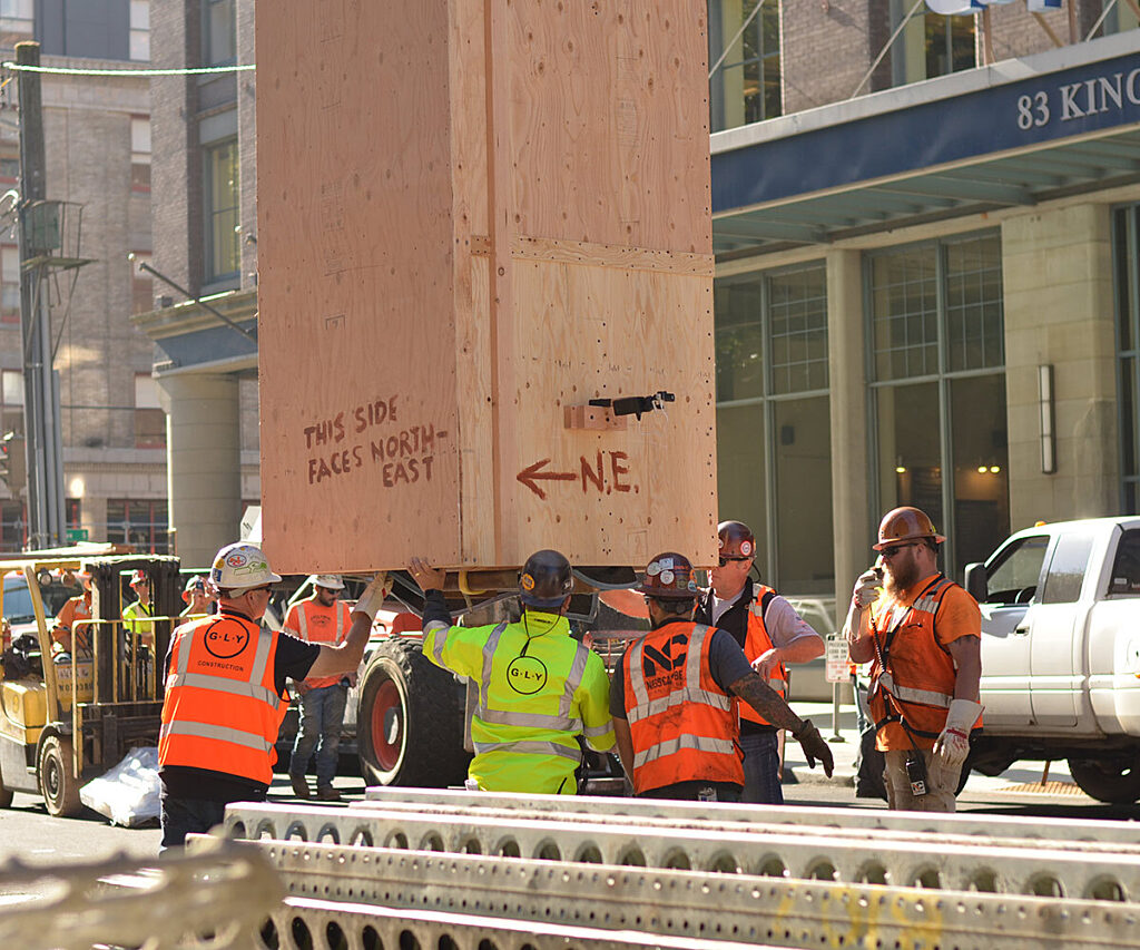 Photo of group of construction workers maneuvering large plywood box