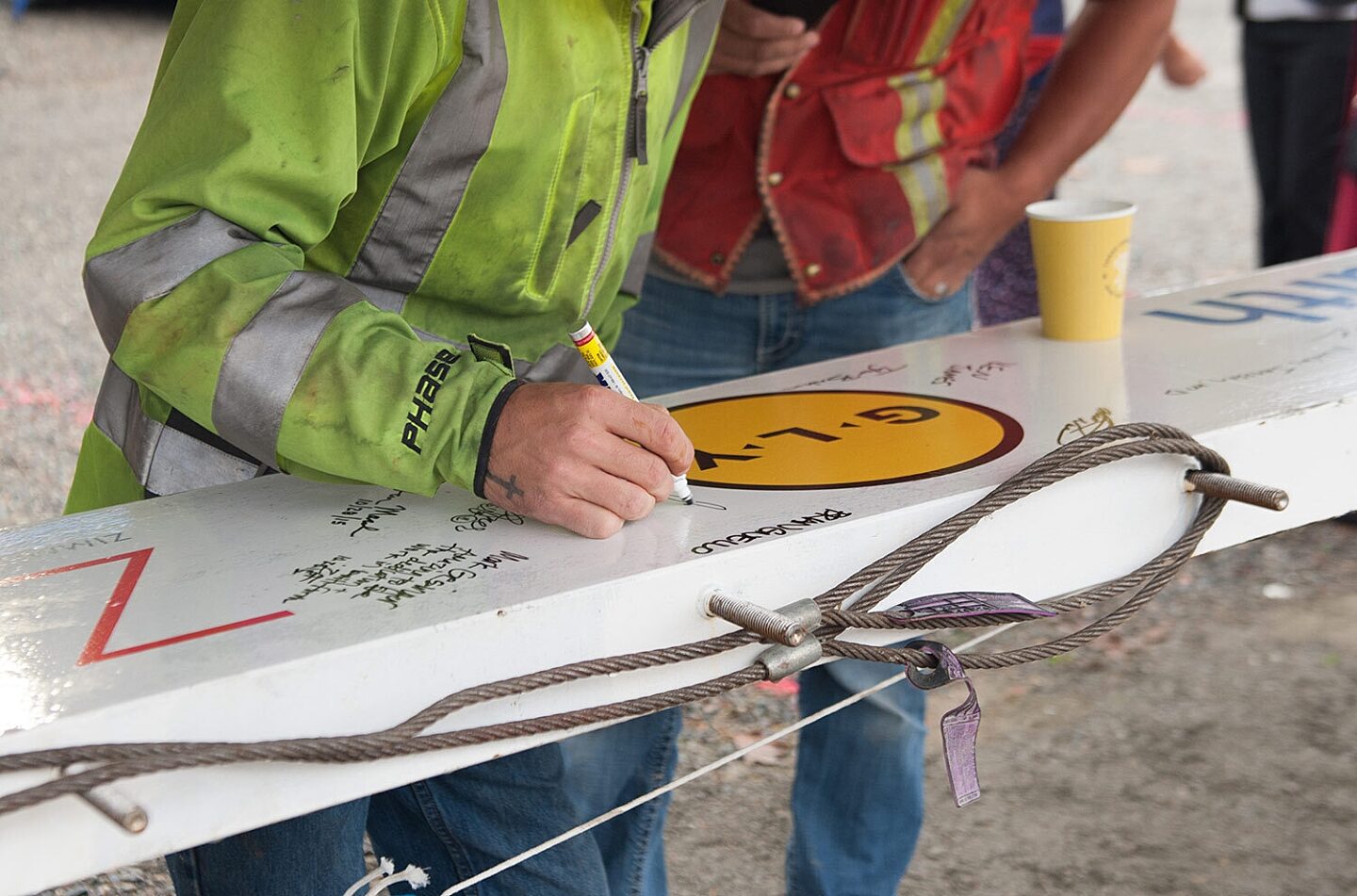 Construction worker signing name on steel beam with GLY logo