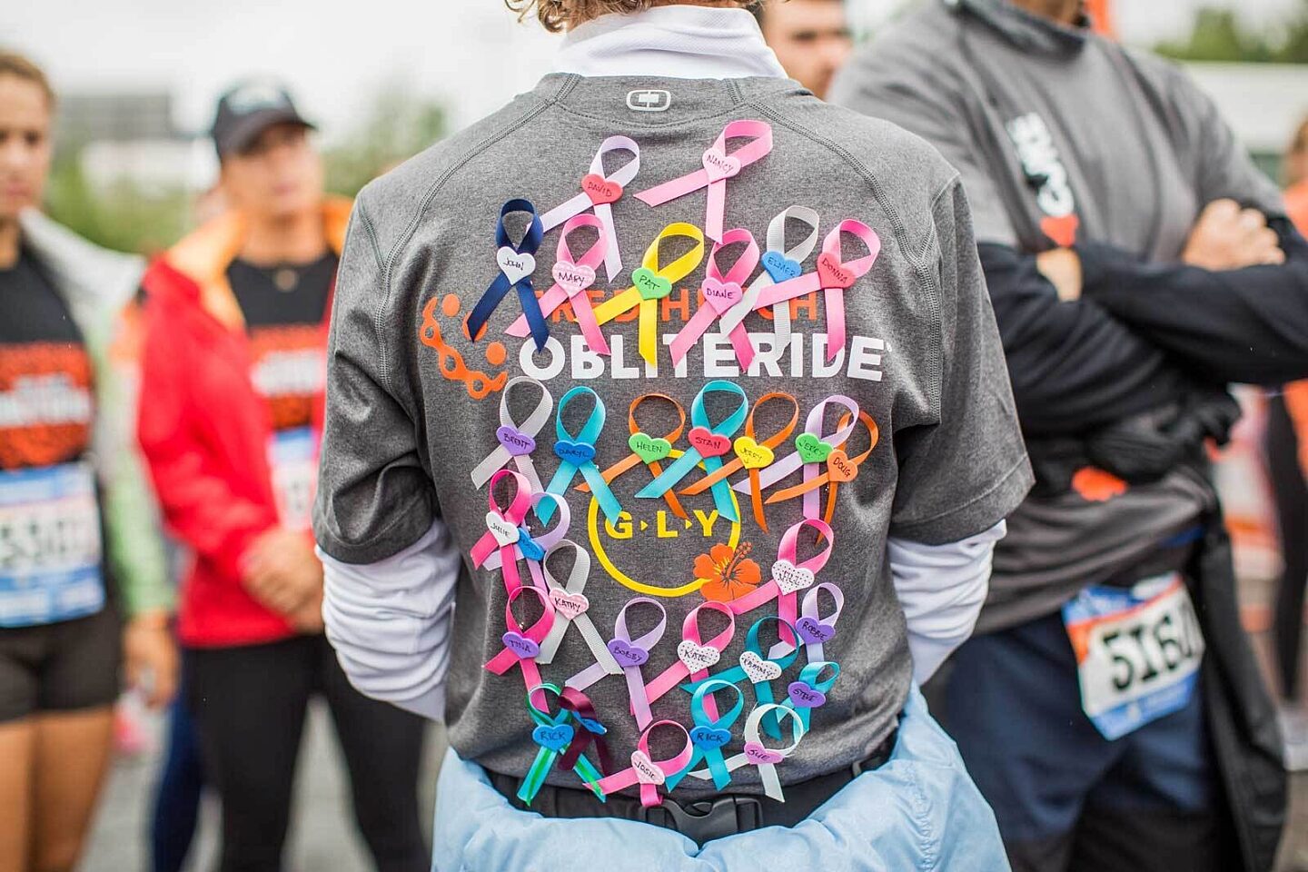 A runner's back with an "Obliteride" shirt with many ribbons pinned to it.