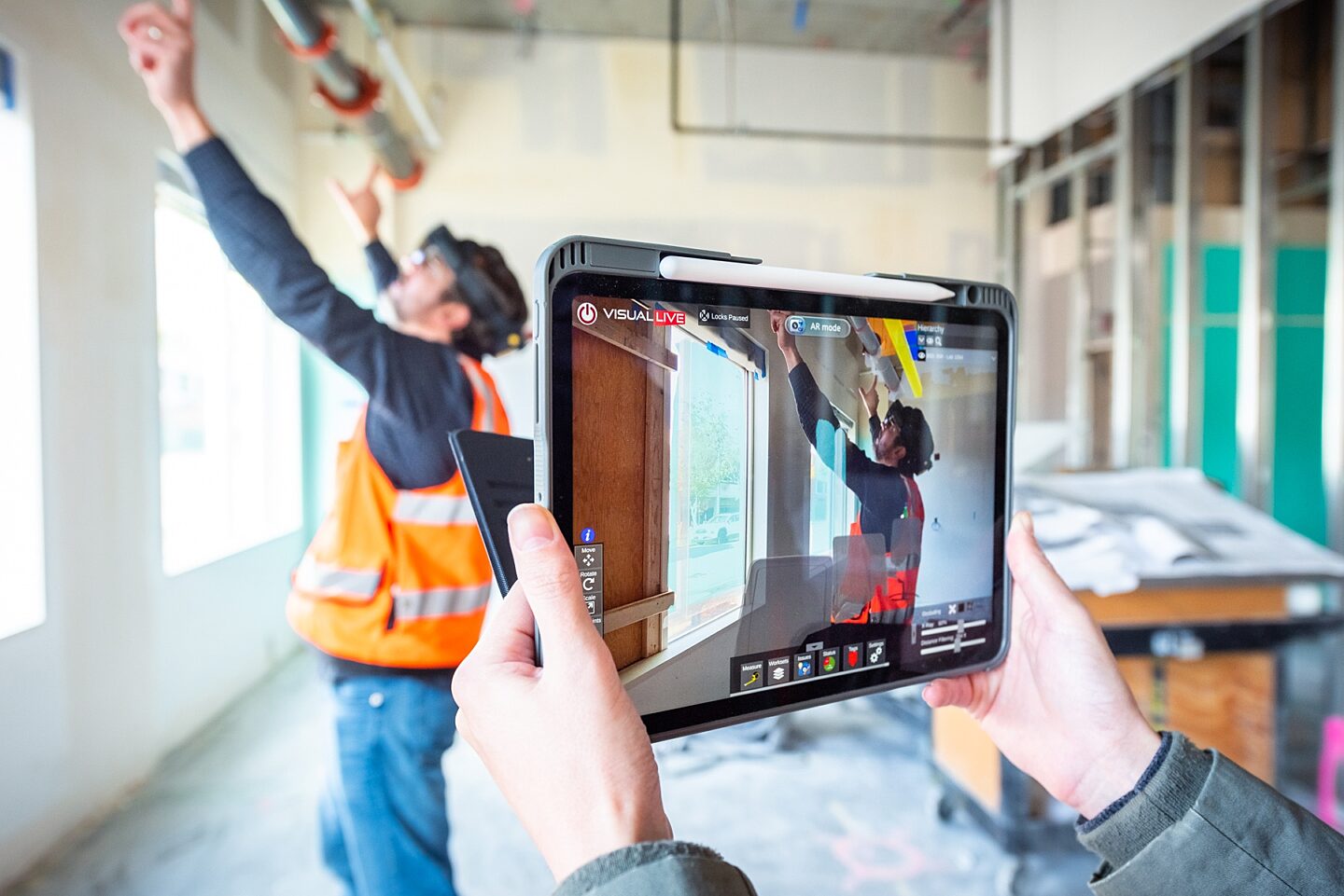 Close-up photo of tablet showing AR technology with construction worker inspecting pipes