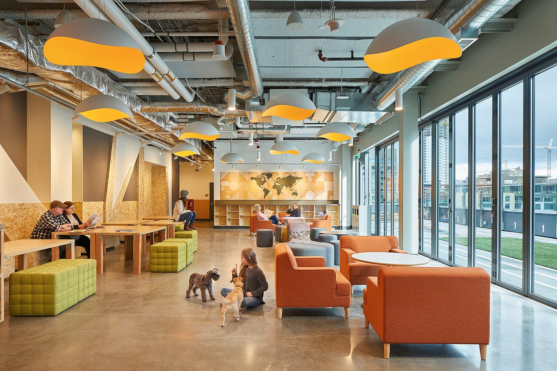 Interior photo of office building common area with people reading and two dogs playing with a child