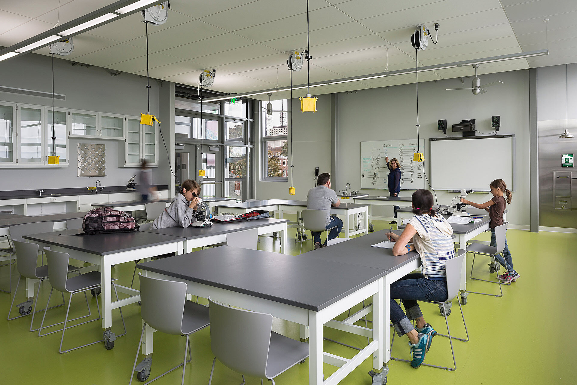 Interior photo of classroom with children sitting at tables and teacher pointing to whiteboard