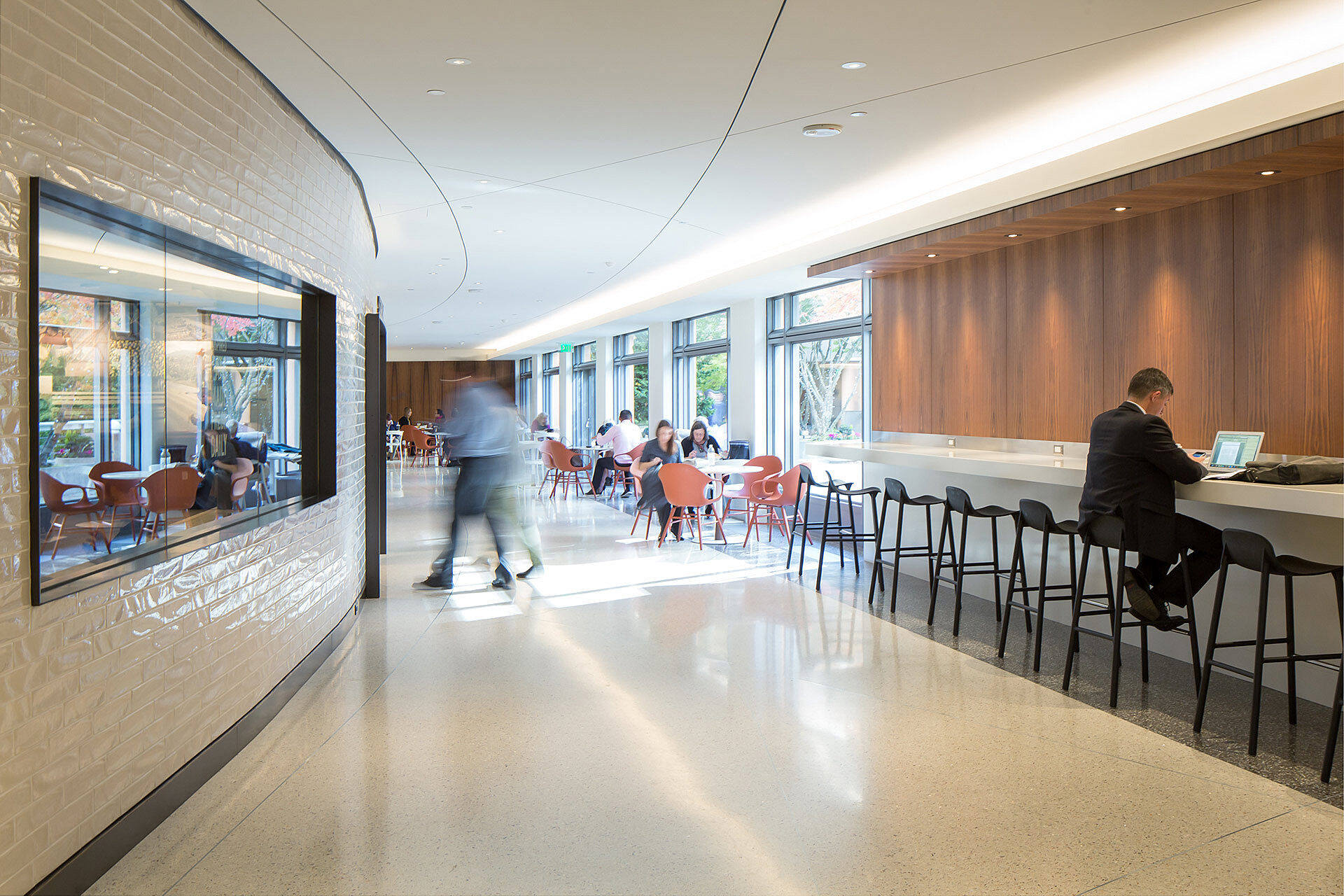 Interior photo of finished building common area space with individuals sitting in chairs and walking