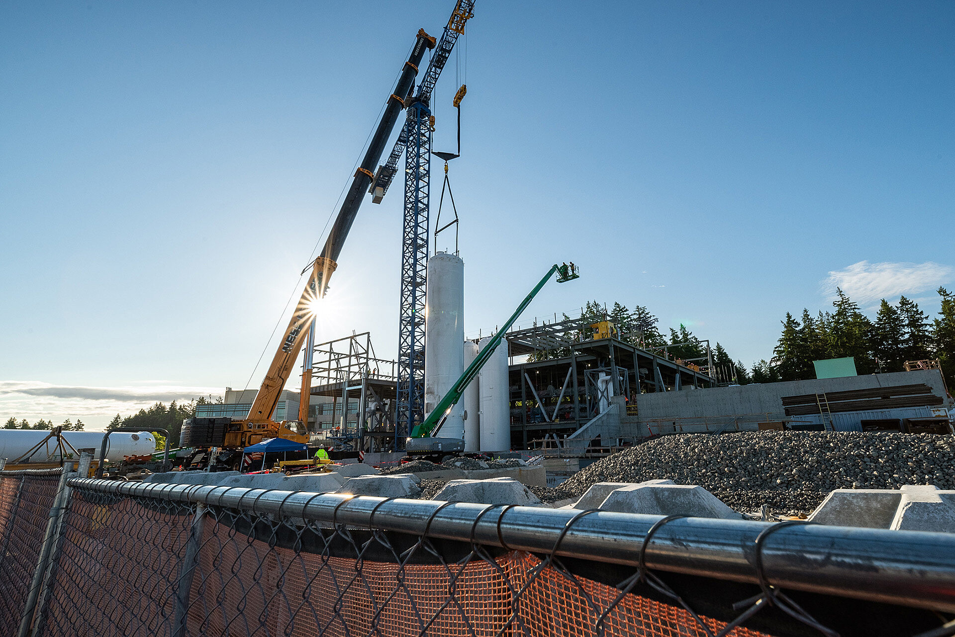Exterior photo of construction jobsite taken behind fence and showing two cranes and manlift