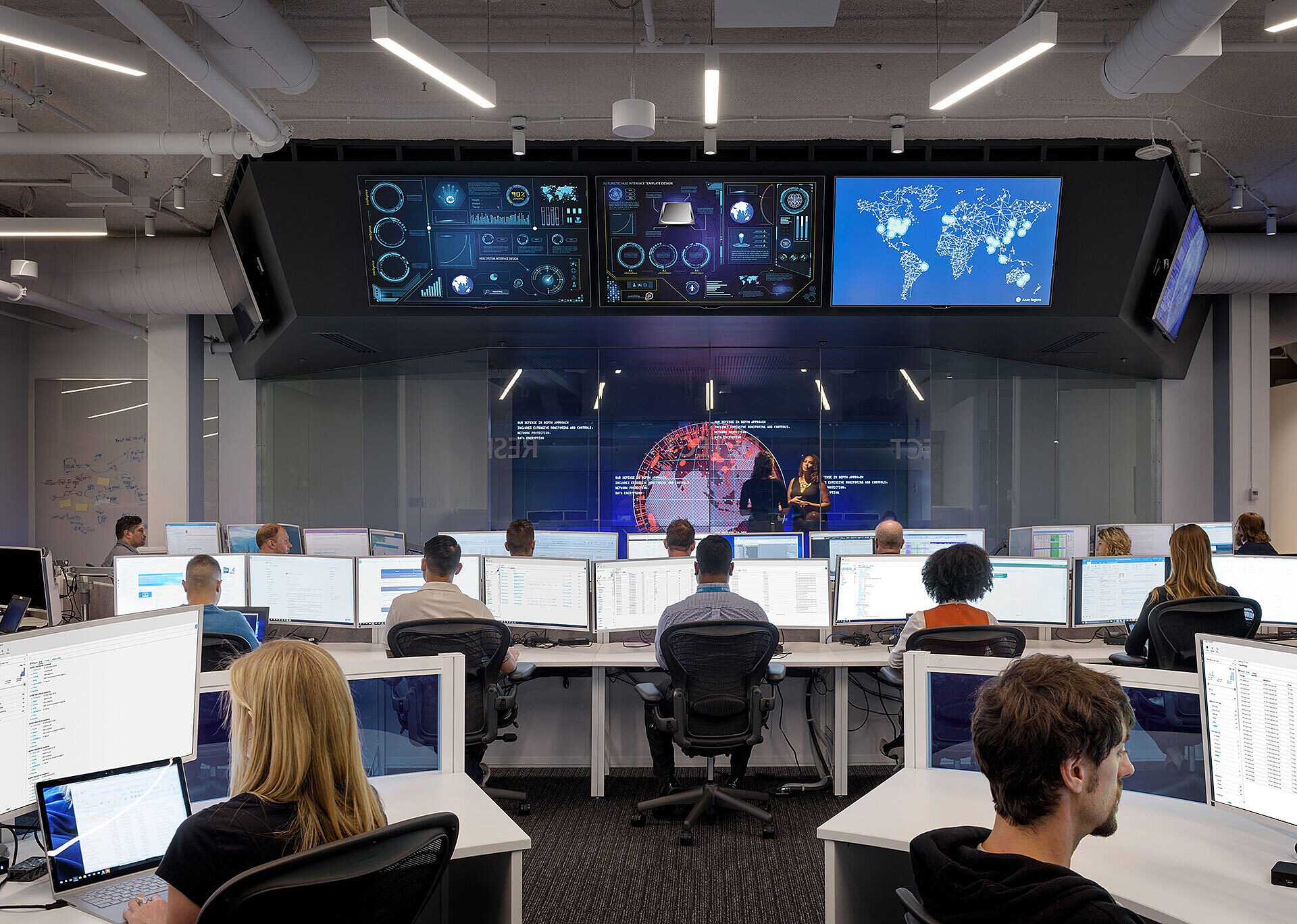 Interior photo of high-tech office space with individuals at computers viewing overhead monitors