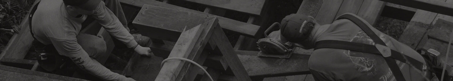 Darkened/stylized background image of construction workers cutting wood