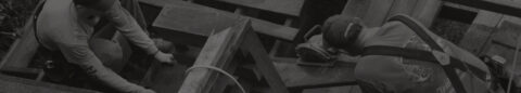 Darkened/stylized background image of construction workers cutting wood